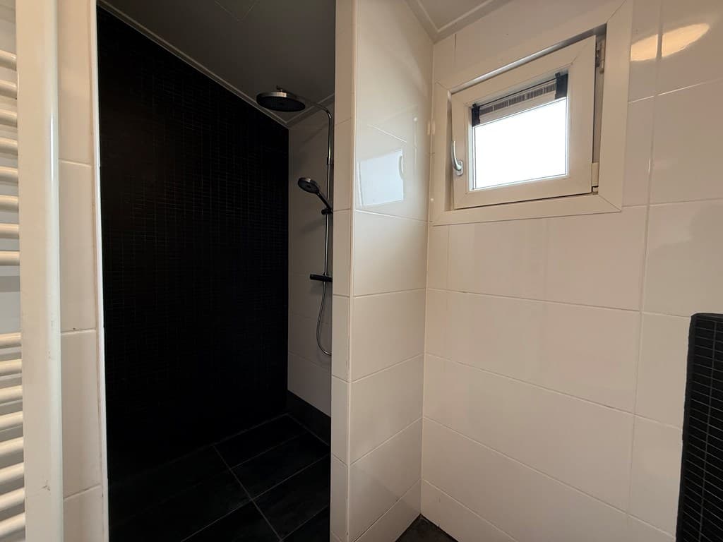 Moderne badkamer met inloopdouche, zwarte wandtegels en een klein raam voor natuurlijk licht