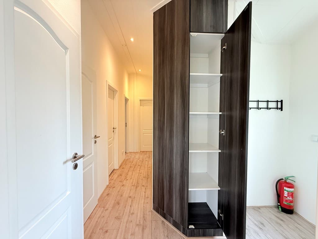 Ingang met houten vloer en kast, lange gang met meerdere deuren en wandhaakjes.
