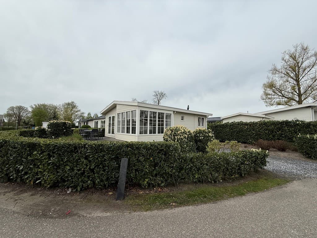 Hoekwoning met grote raampartijen, omringd door groene hagen en een grindpad in EuroParcs De Biesbosch.