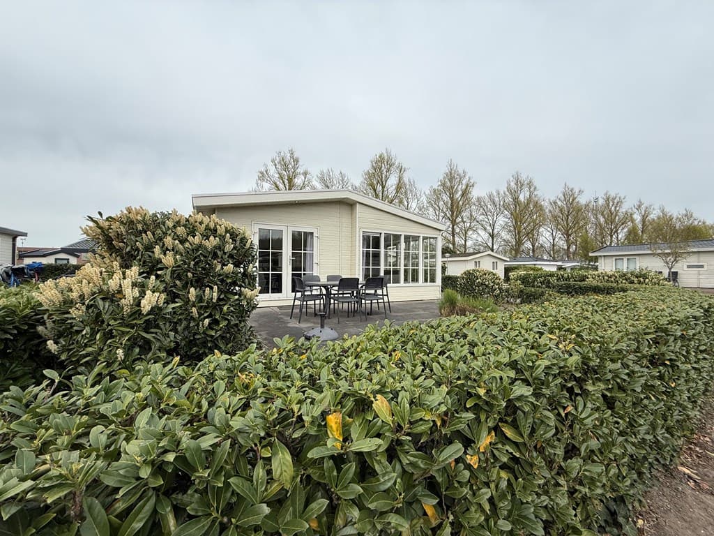 Vakantiewoning met patio en hoge ramen, omringd door haag en uitzicht op bomen in EuroParcs De Biesbosch.