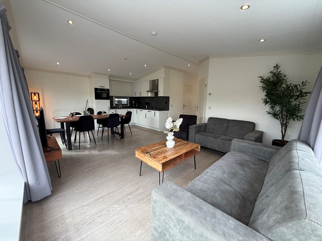 Lichte woonkamer met eet- en zithoek, keuken in open verbinding en een grote raam voor natuurlijk licht.