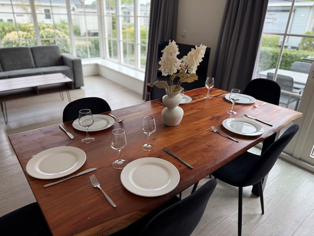 Eettafel met witte borden en glazen, omringd door zwarte stoelen en grote ramen met uitzicht op de tuin