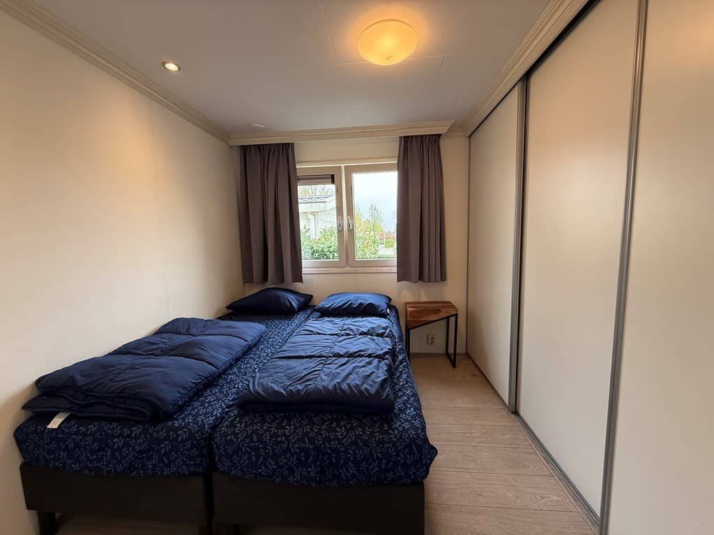 Slaapkamer met twee eenpersoonsbedden, een raam en gordijnen, met een nachttafeltje naast het bed.