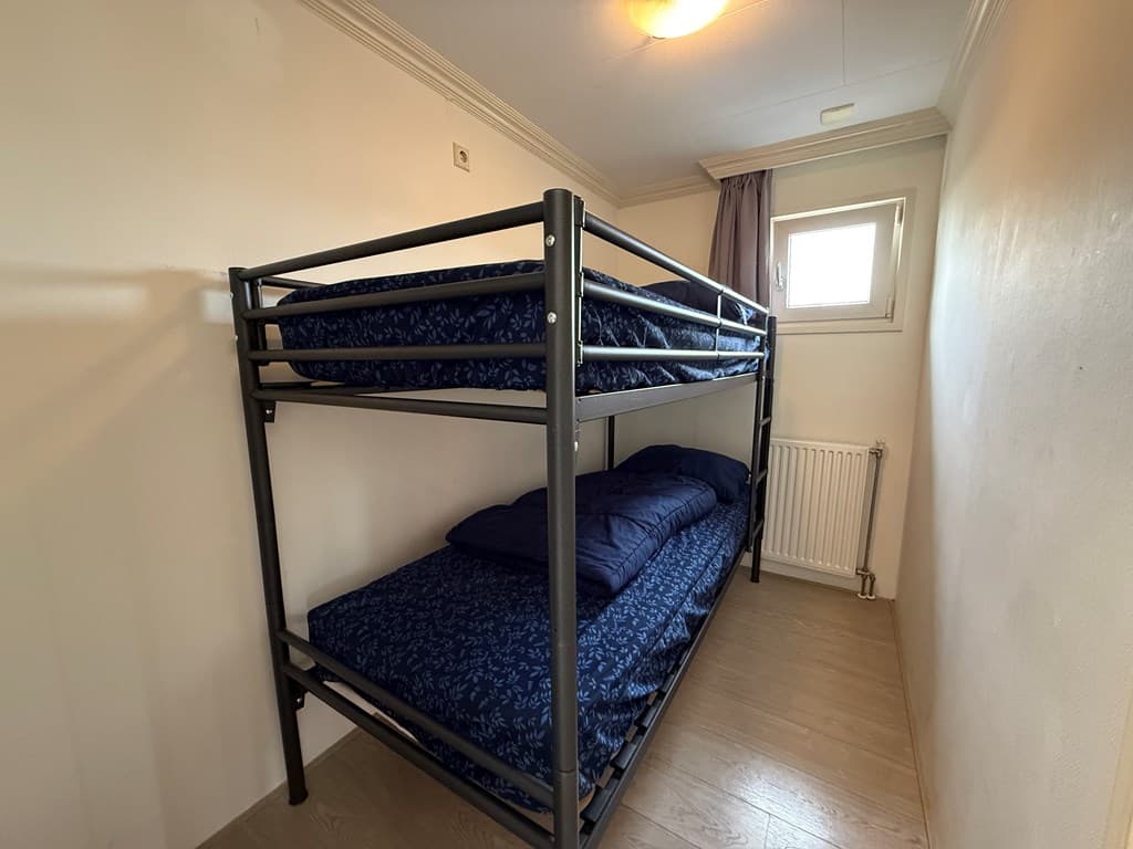 Bunkbed met blauw beddengoed in kamer met vloerbedekking en een raam met gordijn.