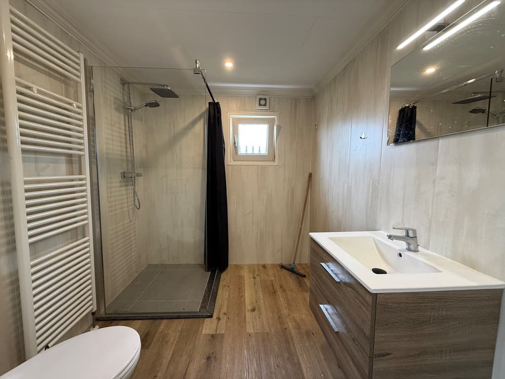 Moderne badkamer met inloopdouche, wastafel met spiegel en vloerverwarming op een houten vloer