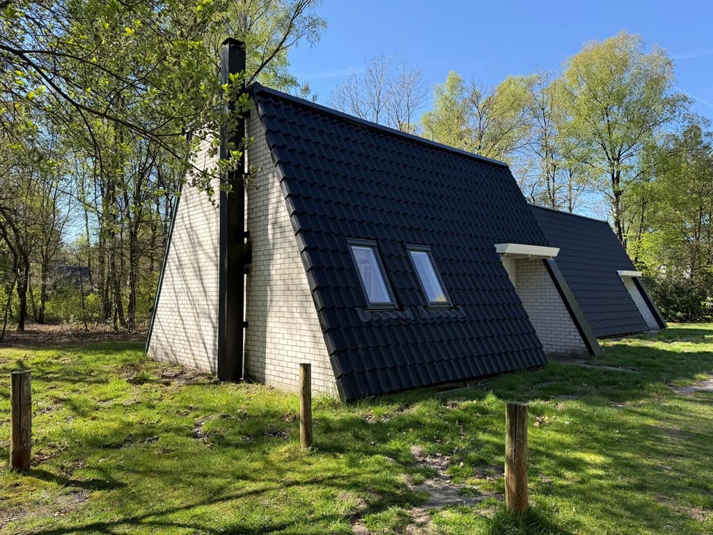 Bungalow met een hellend dak, gelegen in een groene omgeving met bomen en gras rond het pand