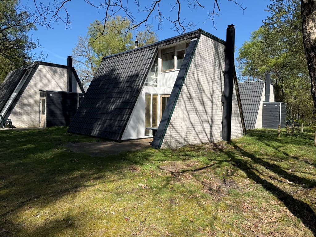 Bungalow met schuin dak, gelegen in een groene omgeving met bomen en een zonnige blauwe lucht