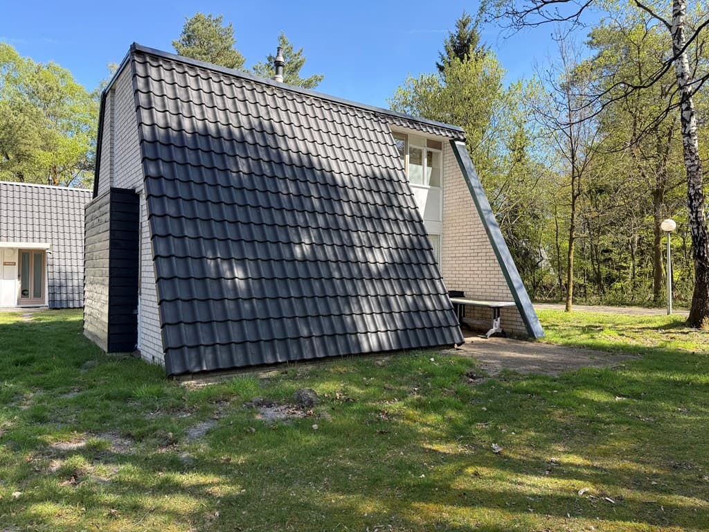Bungalow met een schuin dak, gelegen in een groene omgeving met bomen en gras.