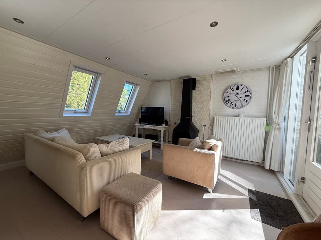 Helle woonkamer met grote raampartijen, banken, een tv en een open haard in Bungalowpark Hoenderloo.