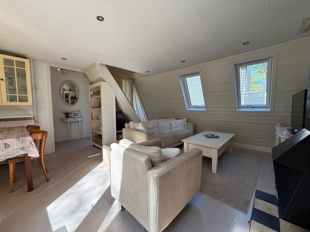 Woonkamer met bank, fauteuils, eettafel en open trap onder een schuin dak metdakramen en lichtinval