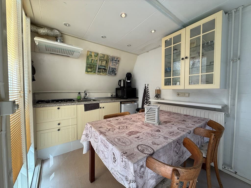 Keuken met een eettafel, stoelen, kastjes en apparatuur zoals een kookplaat en koffiezetapparaat.