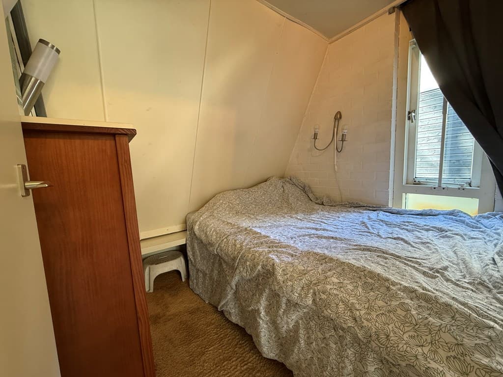 Slaapkamer met een tweepersoonsbed en een houten kast, ramen met vensterbank en beige vloerkleed.