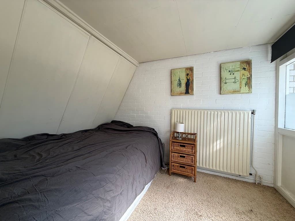 Slaapkamer met een eenpersoonsbed, radiator, nachtkastje en schilderijen aan de muur.