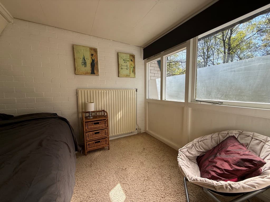 Slaapkamer met een bed, radiator, een wandkast en grote ramen met uitzicht op een groene omgeving