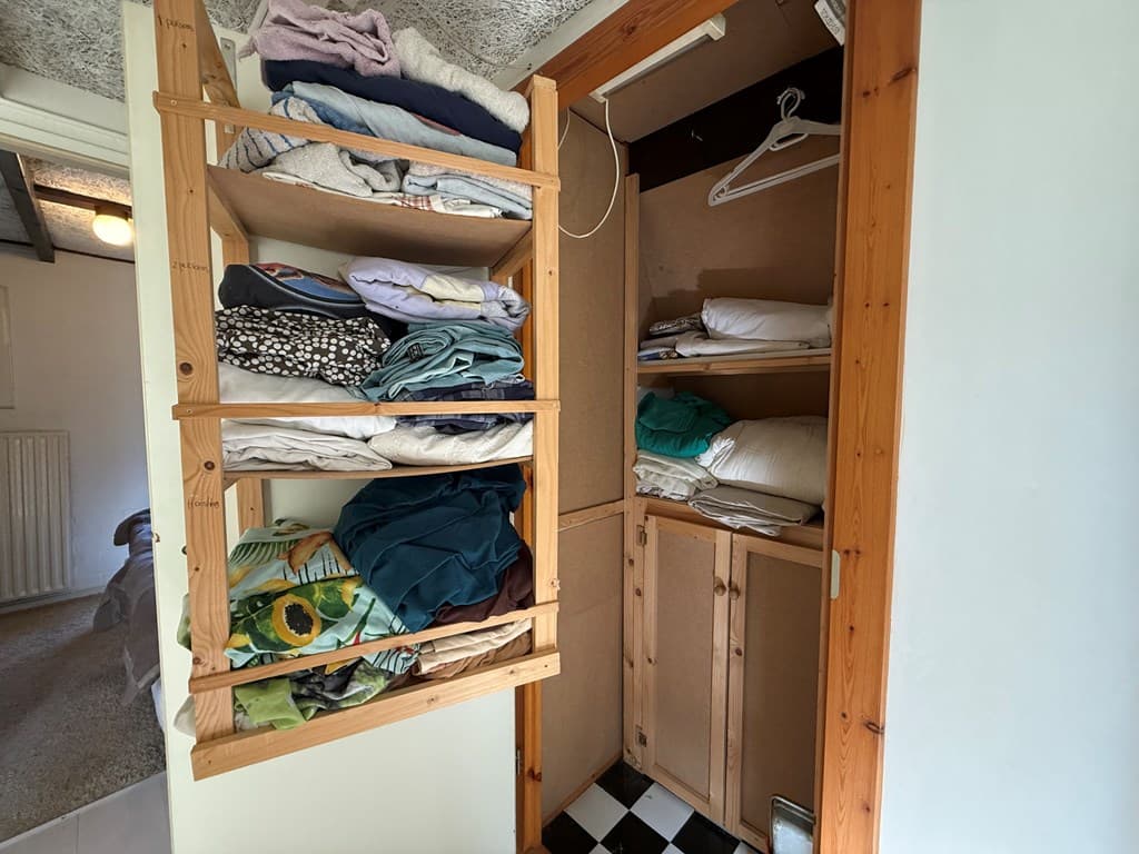 Ingerichte kast met opbergplanken vol met schone lakens en handdoeken, en een onderste kast met deuren.