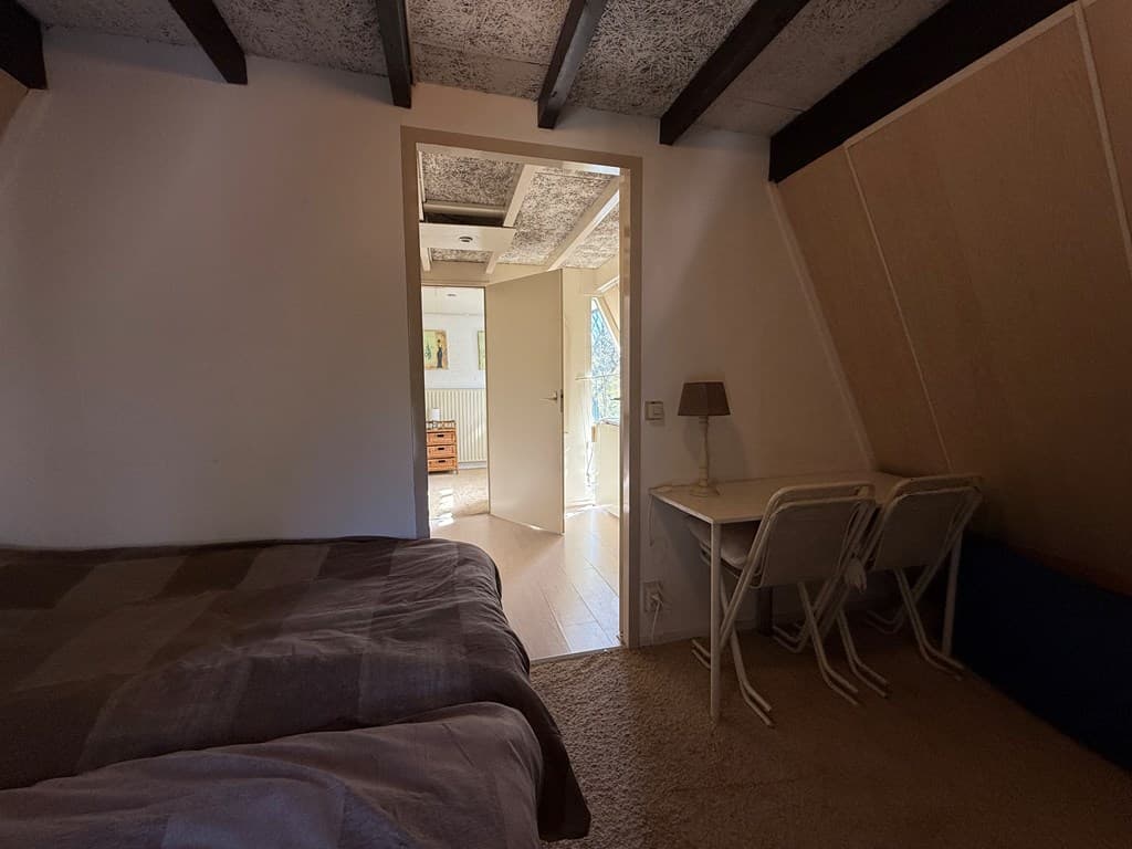 Slaapkamer met twee eenpersoonsbedden en een klein bureau, uitzicht op een doorgang naar een lichte ruimte.