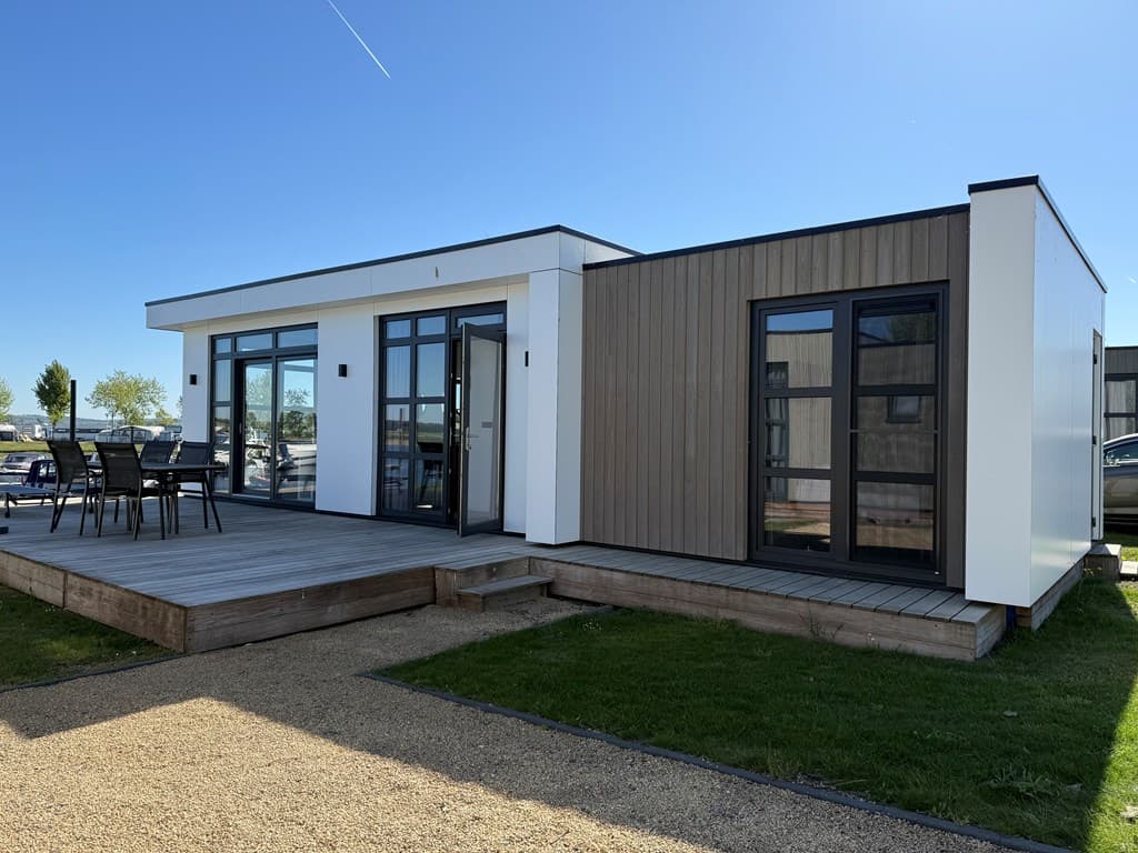 Moderne vakantiewoning met houten gevel, grote ramen en een terras met tuintafel en stoelen.