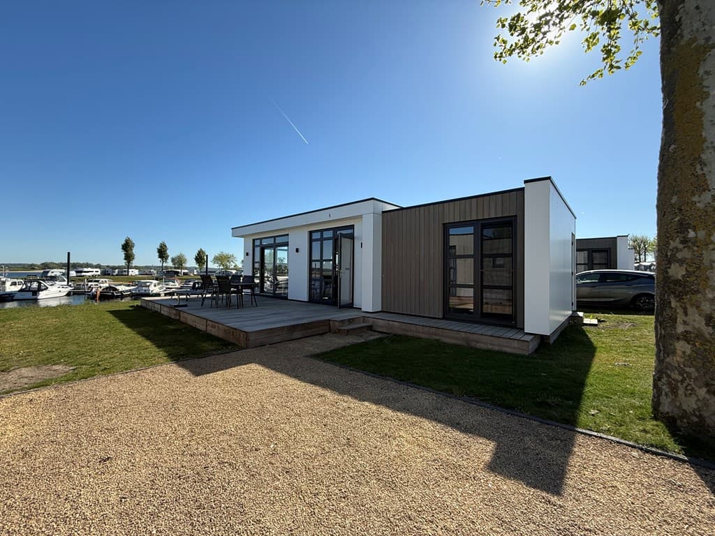 Moderne vakantiewoning met houten terras en uitzicht op de jachthaven, omgeven door gras en enkele bomen
