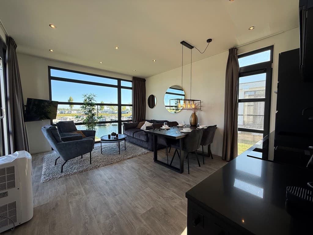 Moderne woonkamer met uitzicht op het water, groot raam, comfortabele zithoek en eettafel met vier stoelen