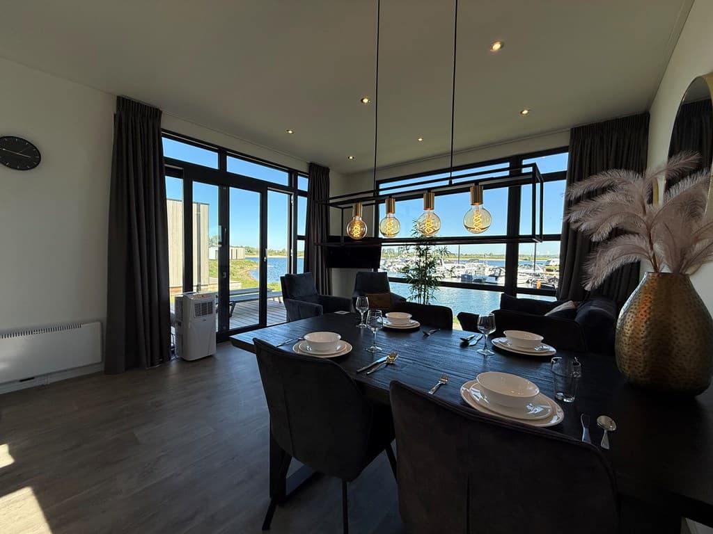 Eetkamertafel met zes stoelen, grote ramen met uitzicht op de haven en moderne verlichting boven de tafel