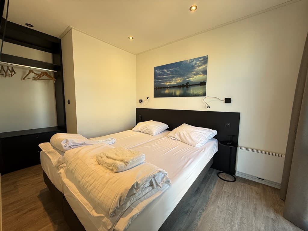 Slaapkamer met twee eenpersoonsbedden, wandkast en een schilderij van een waterlandschap.