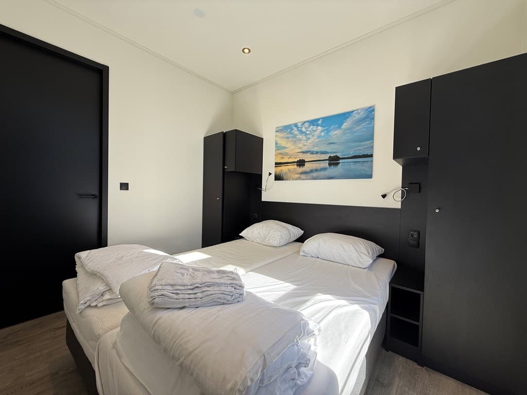 Slaapkamer met twee eenpersoonsbedden, zwarte kasten en een schilderij met een landschap aan de muur.