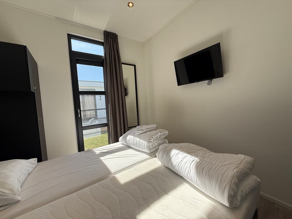 Slaapkamer met twee eenpersoonsbedden, grote ramen en een televisie aan de muur.