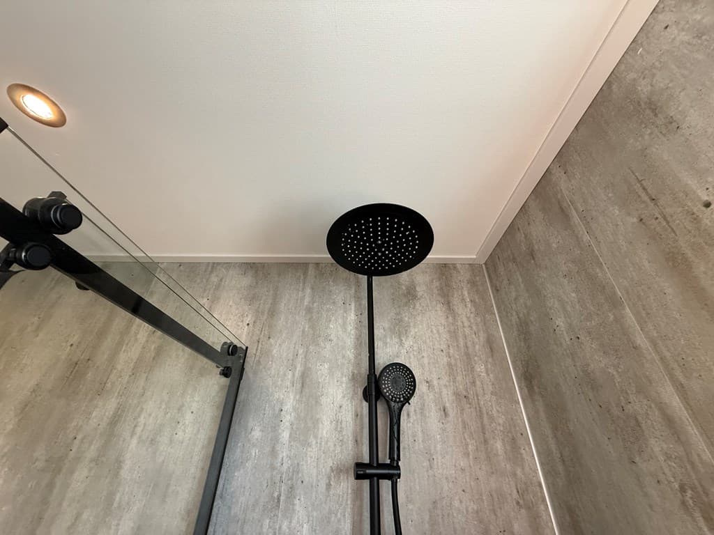 Moderne douche met een zwarte regendouche en handdouche in een betegelde ruimte met lichte muren.