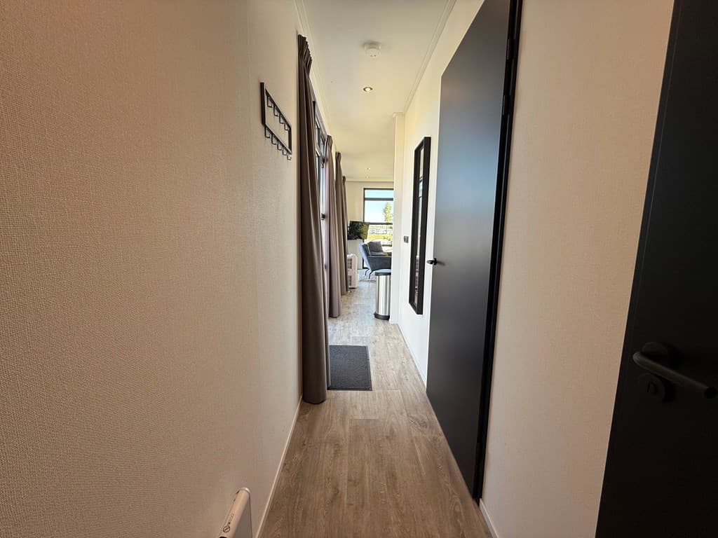 Lichte gang met een deur aan de rechterkant en toegang tot een woonkamer met uitzicht op buiten.