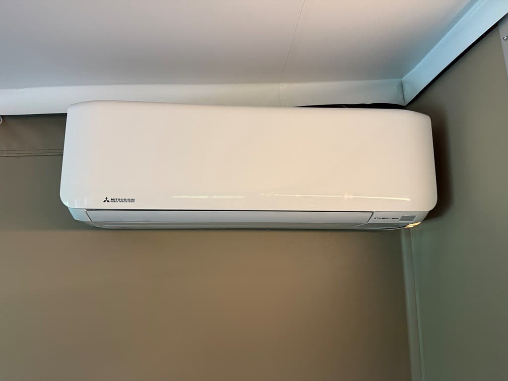 Airconditioner aan de muur in een lichte ruimte met een groene wand.