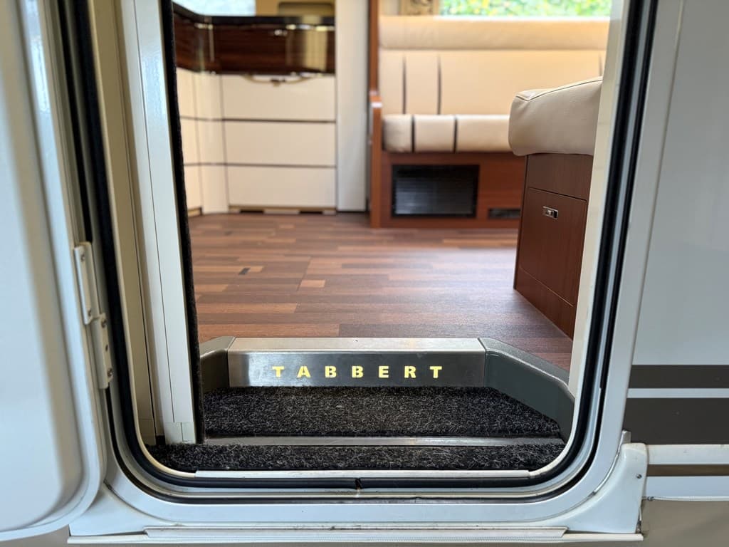 Ingang van een caravan met een tapijt bij de deur en de naam 'TABBERT' zichtbaar op de trede.