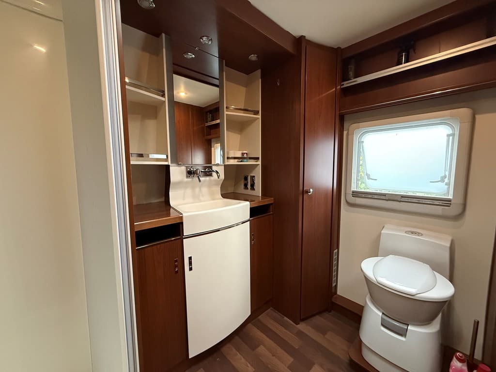 Moderne badkamer met houten kasten, wastafel en toilet, raam met uitzicht naar buiten.