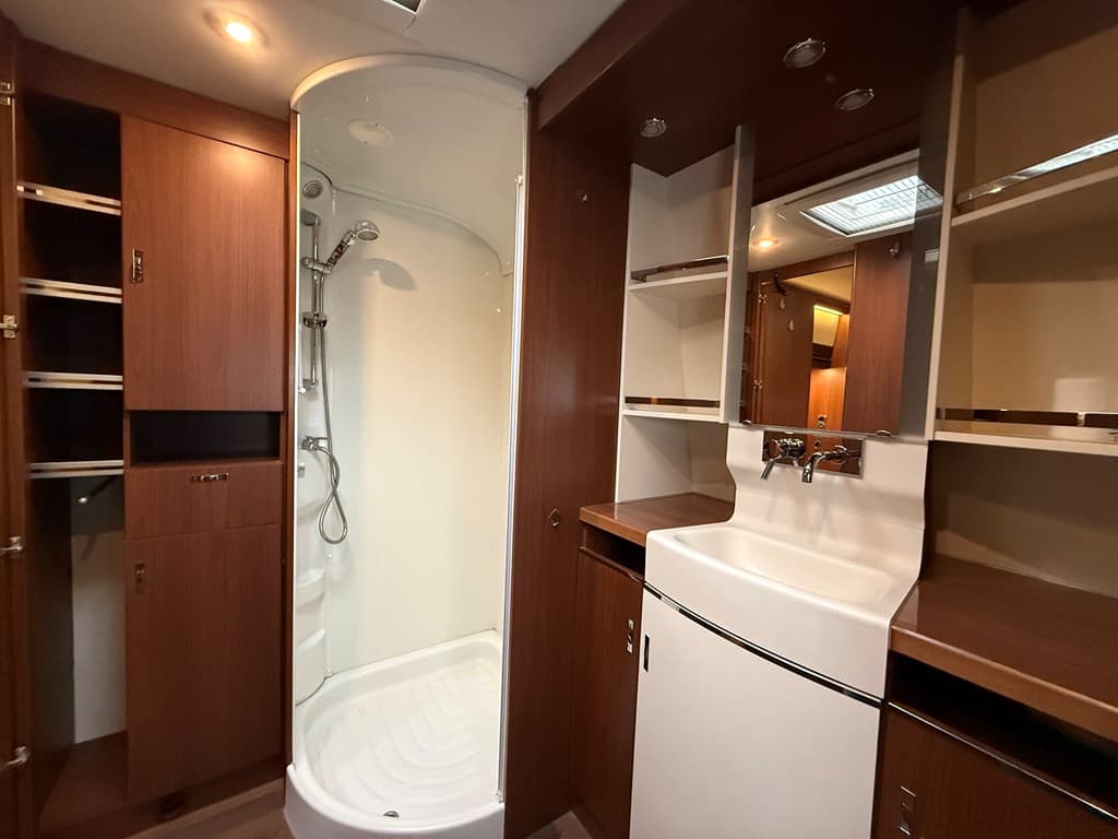 Ingerichte badkamer met douche, wastafel en kasten in warme houtkleuren.