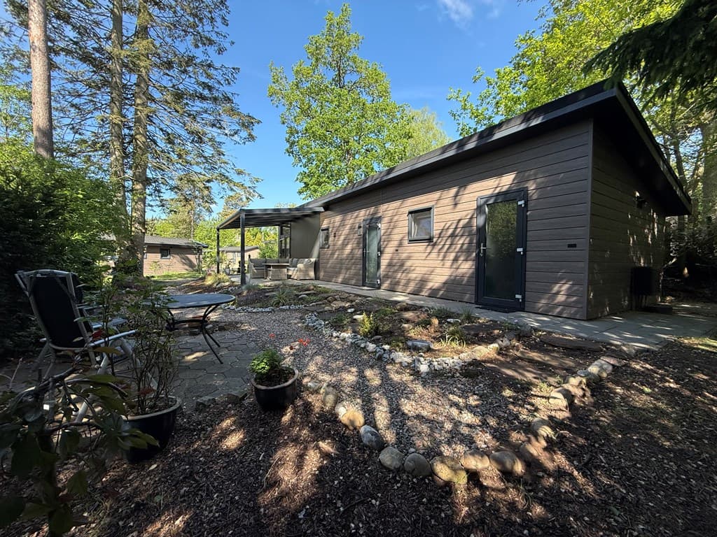 Moderne vakantiewoning omgeven door groen, met stenen pad en terras, en een eigen tuin met beplanting.