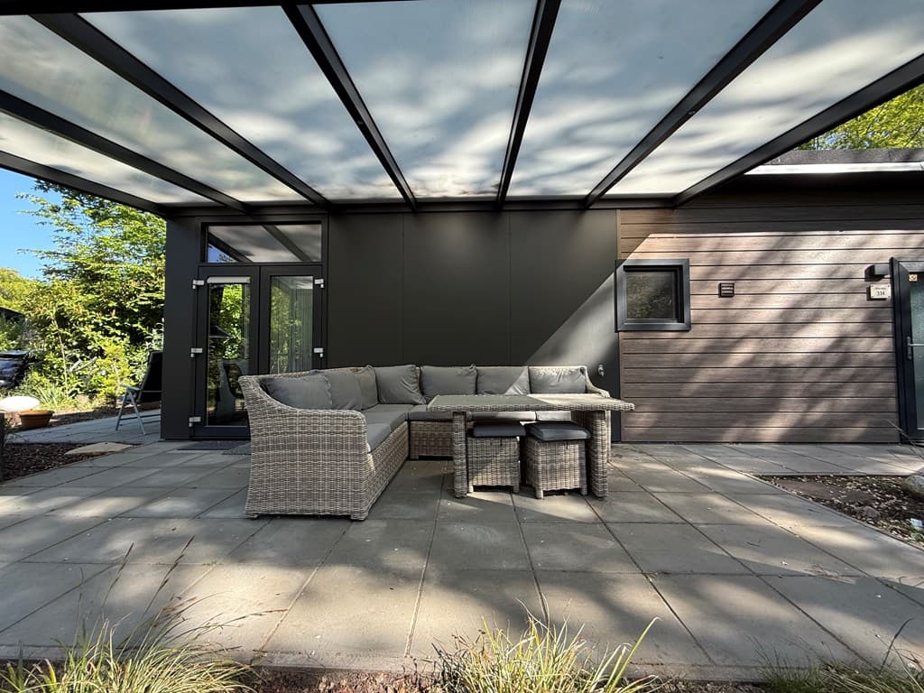 Terras met comfortabele zithoek onder een glazen overkapping en moderne gevel van een woning in Veluwepark de Bosgraaf.