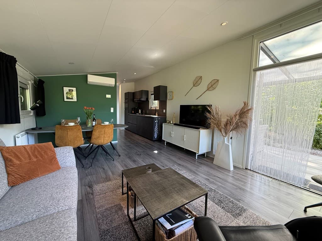 Modern interieur met zithoek, eettafel en open keuken, grote ramen zorgen voor veel lichtinval.