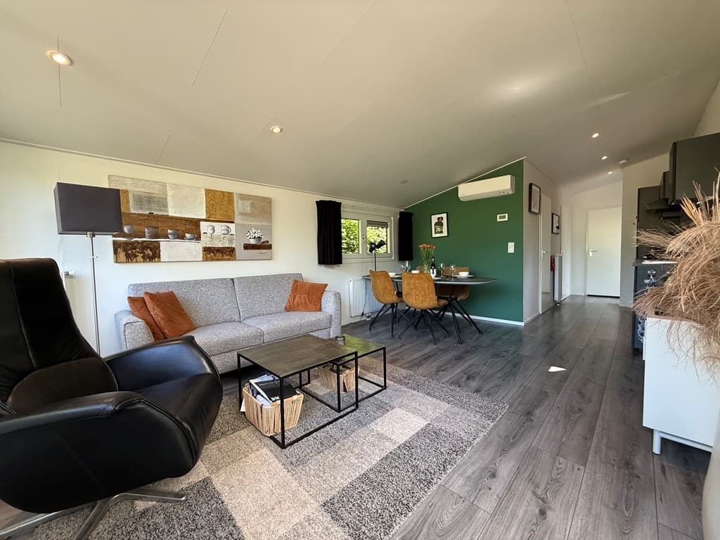 Moderne woonkamer met een zithoek, eettafel, groene wand en houten vloer in een vakantiewoning