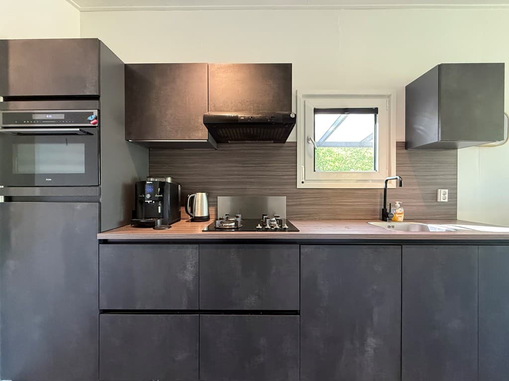 Moderne keuken met zwarte kasten, inbouwapparatuur en een houten werkblad in lichte ruimte