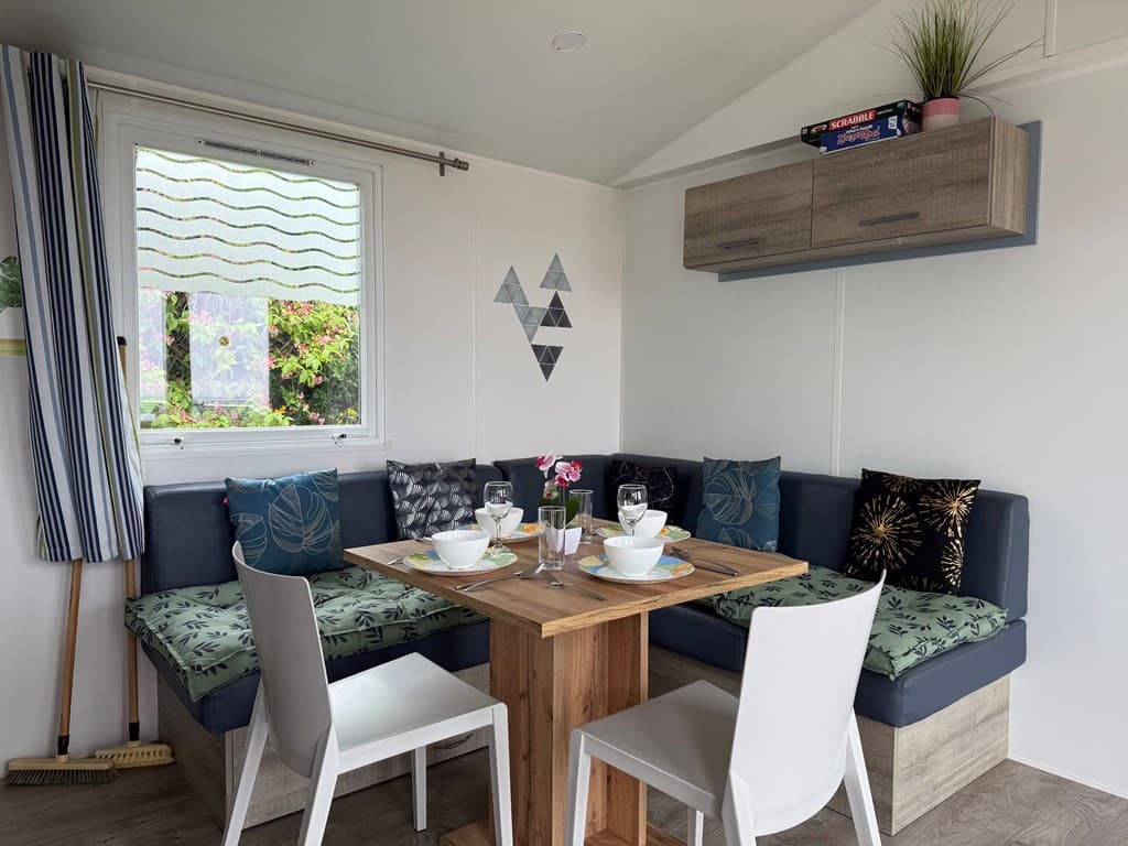 Eettafel met banken in een lichte kamer, verschillende kussens en planten op de plank aan de muur