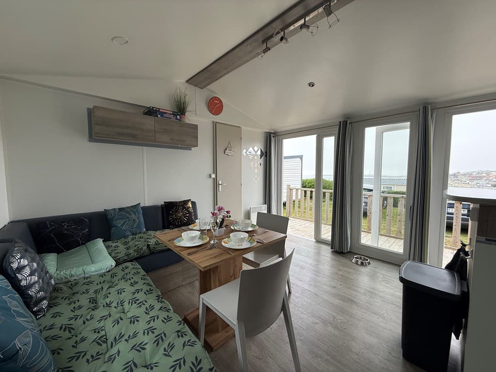 Gezellig interieur met zithoek, eettafel en grote ramen met uitzicht op buitenruimte en omgeving.