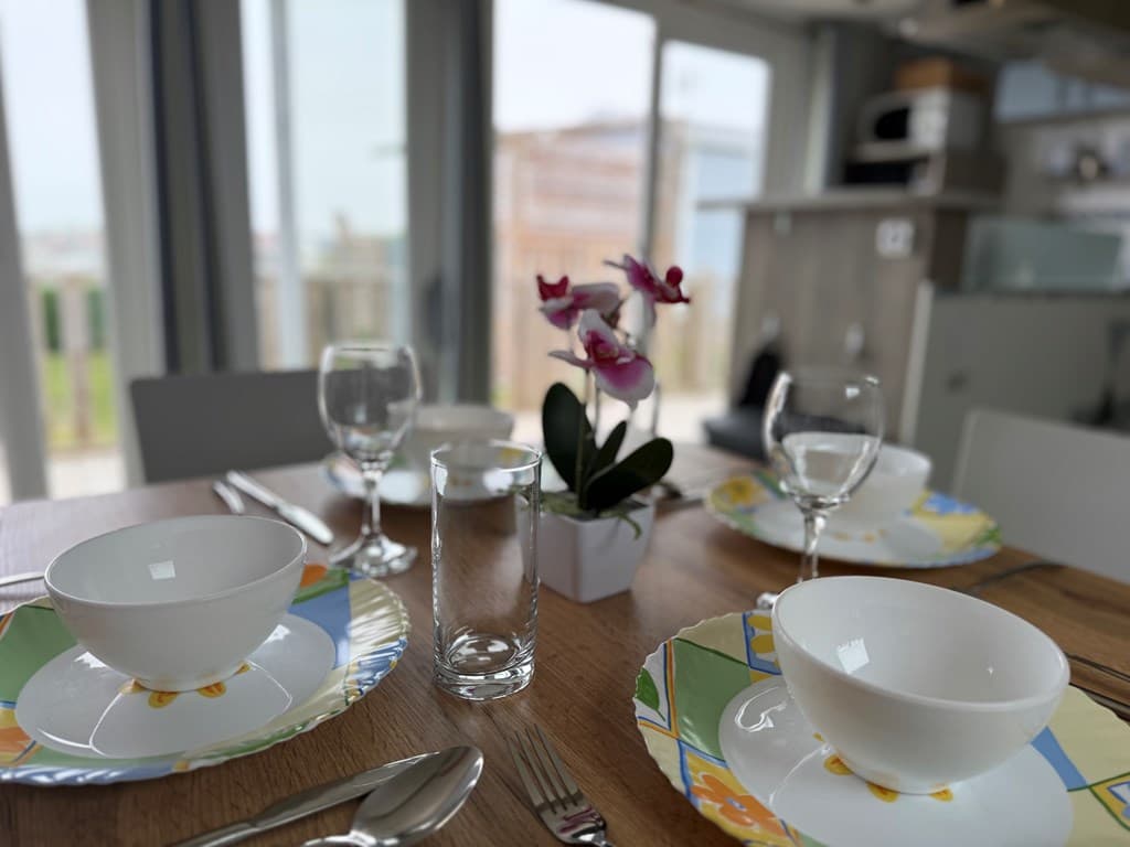 Eetkamertafel gedekt met servies en glazen, uitzicht op groene omgeving door raam op de achtergrond