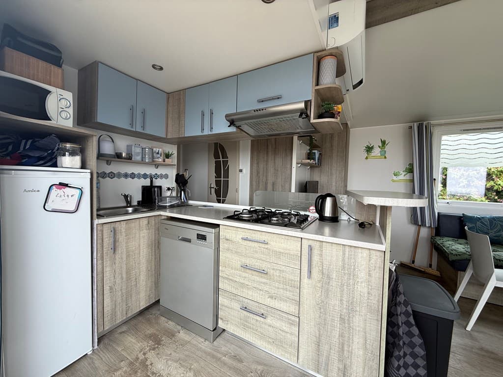 Moderne keuken met houten kasten, gasfornuis, koelkast en zithoek met ramen en planten aan de muur