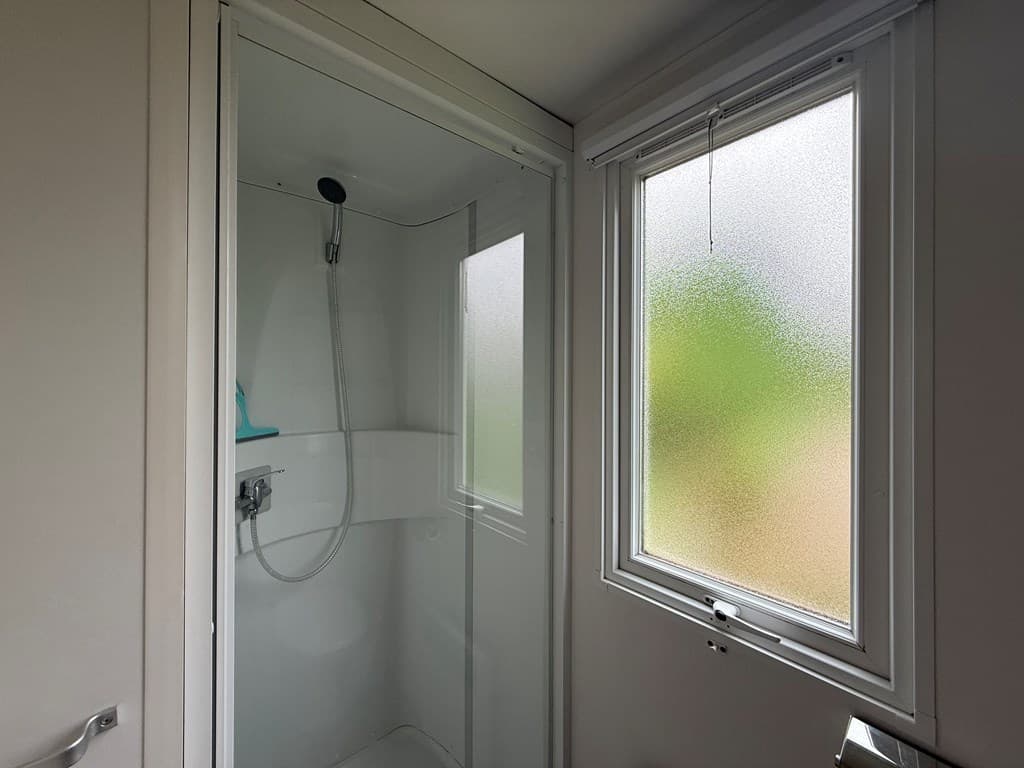 Douchecabine met glazen deur en een raam met een matte afwerking, lichte wanden en een eenvoudige inrichting