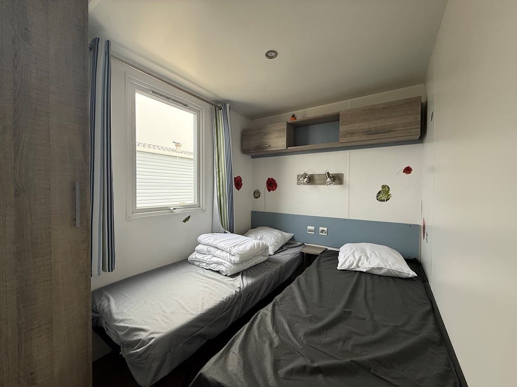 Slaapkamer met twee bedden, raam met gordijnen en wanddecoratie van bloemen. meubel met verlichting aan de muur.