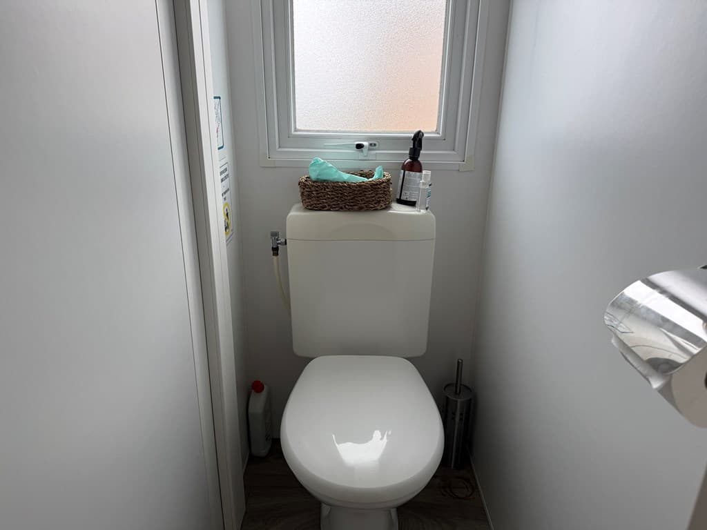 Toilet met staand sanitair, raam met gestructureerd glas en enkele accessoires op de toiletcistern.