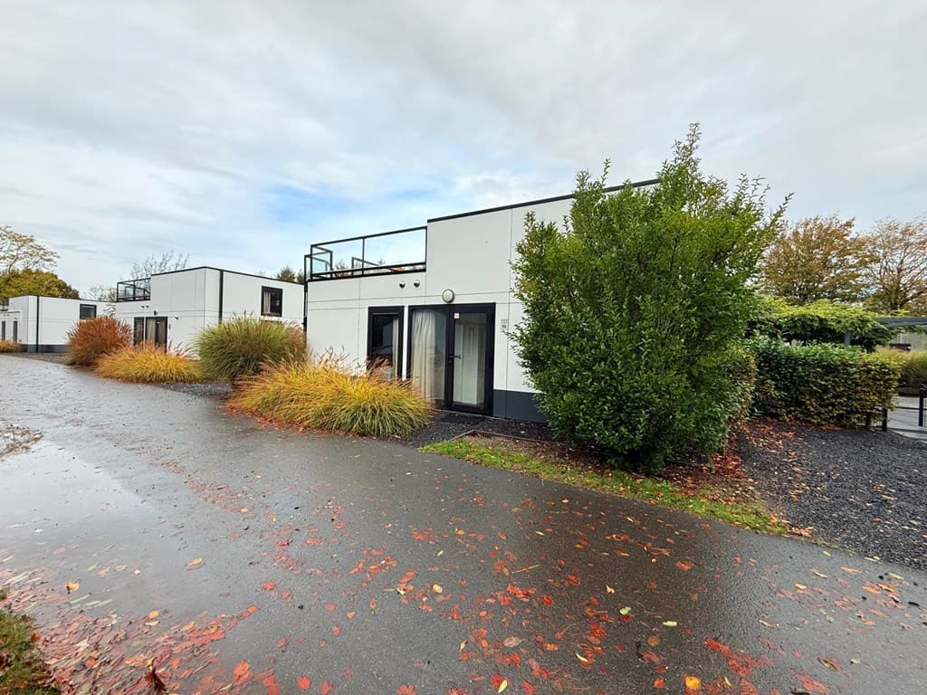 Moderne vakantiewoning met groene beplanting en paden van asfalt en grind, onder een bewolkte lucht