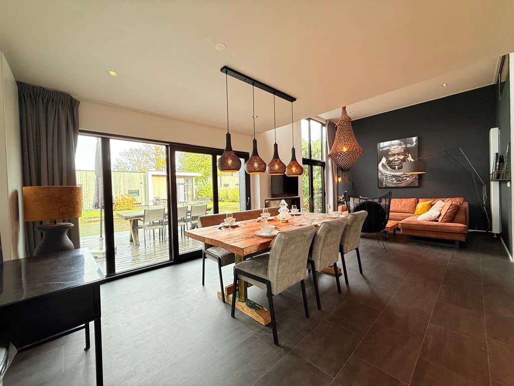 Moderne woonkamer met eettafel en zithoek, grote glazen deuren naar het terras en decoratieve lampen aan het plafond
