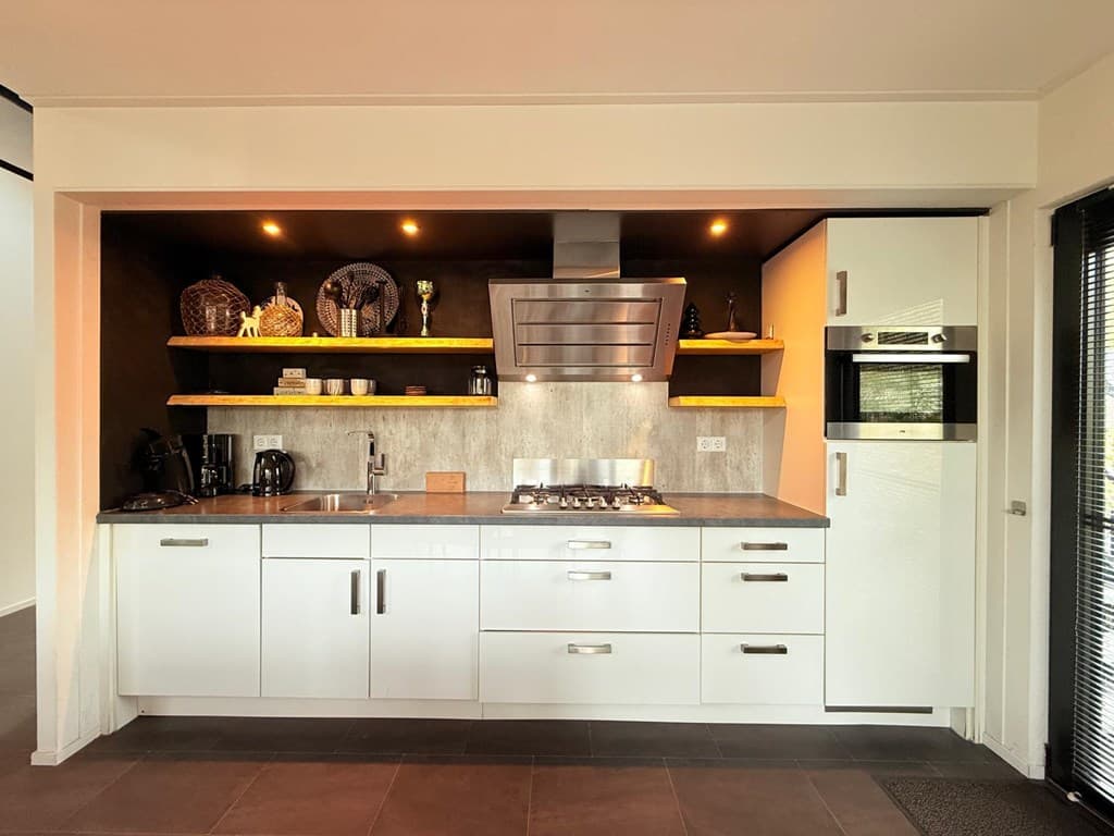 Moderne keuken met witte kastjes, stalen werkblad en inbouwapparatuur, inclusief een gasfornuis en oven.