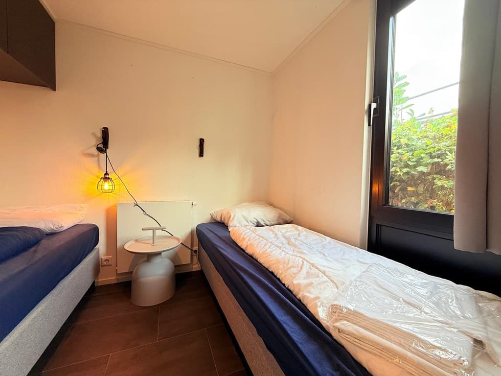 Slaapkamer met twee eenpersoonsbedden, nachttafel en raam met uitzicht op groen buiten.