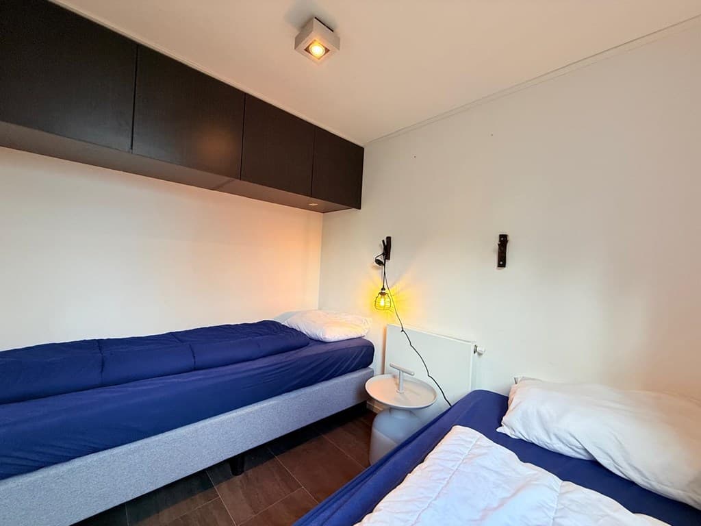 Slaapkamer met twee eenpersoonsbedden, wandlamp en kast boven het bed, neutrale muren en vloer.